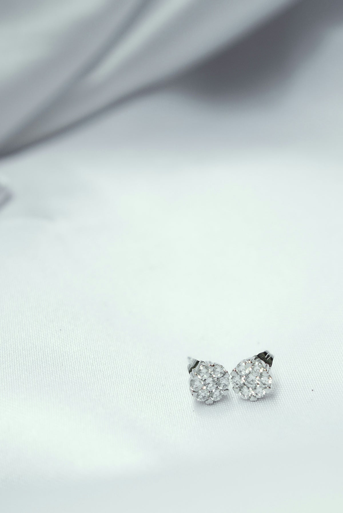 a pair of diamond earrings sitting on top of a white cloth